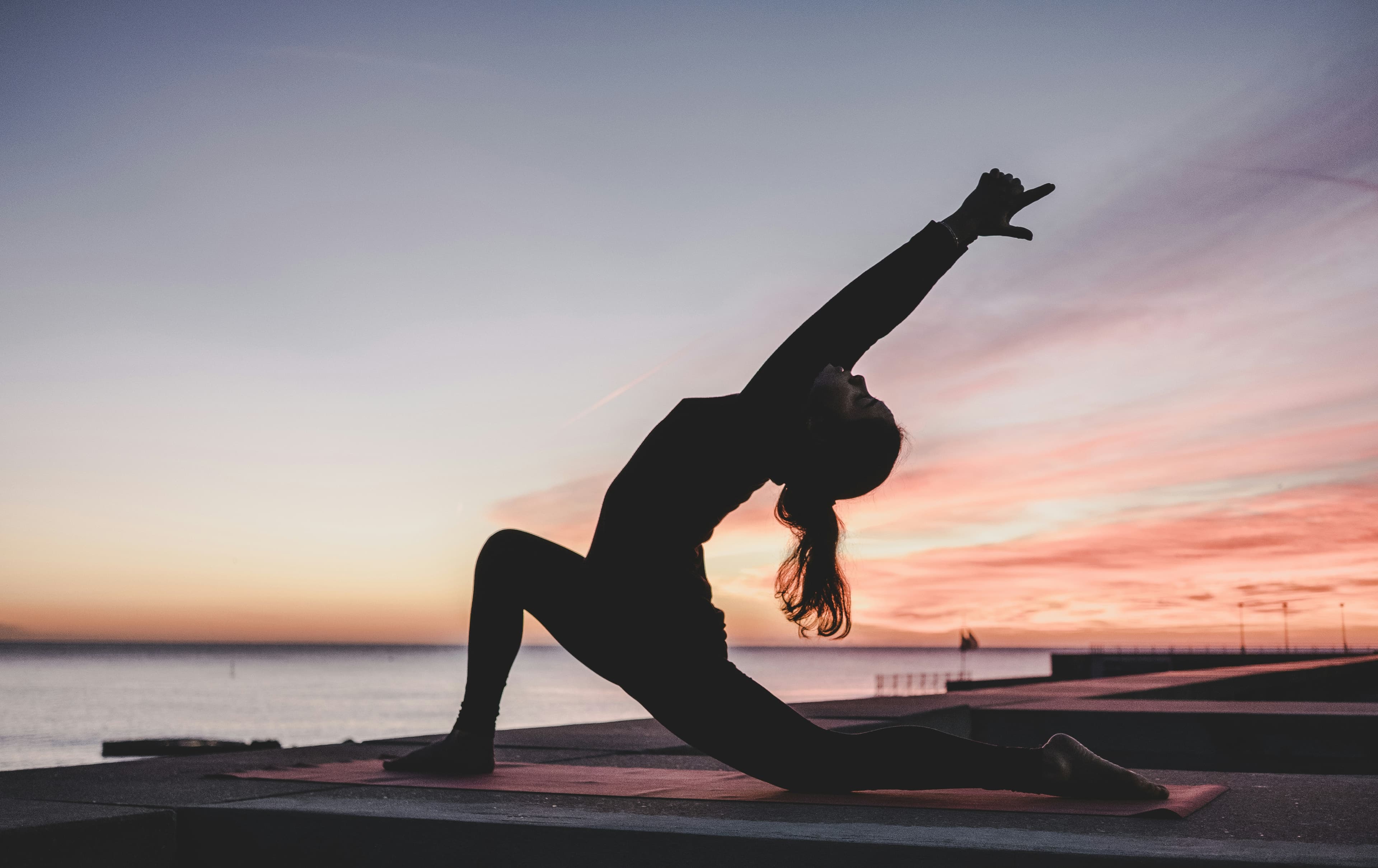Silhouette of a woman in a low lunge yoga pose against a vivid sunset sky by the ocean